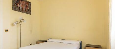 A bedroom with a bed, bedside tables, a floor lamp, and a painting on the wall.