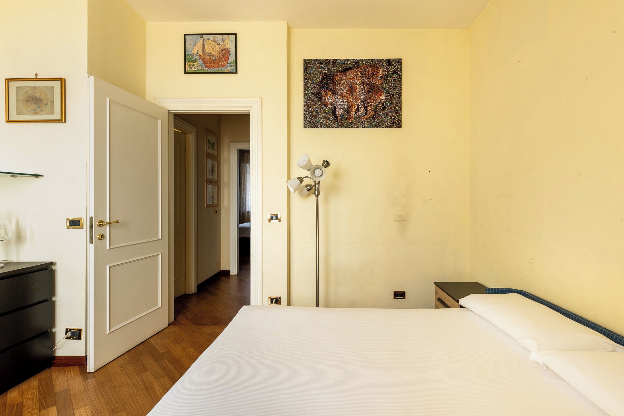 Une chambre d’hôtel avec un lit, une table de chevet, une lampe et une porte donnant sur un couloir.