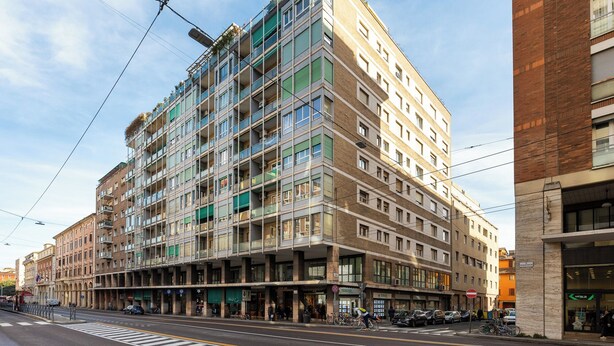 Un edificio de varios pisos con espacios residenciales y comerciales, que cuenta con balcones, ventanas amplias y una entrada a nivel de calle con tiendas.