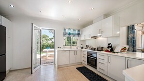 A modern kitchen with white cabinets, a built-in oven, and a large window overlooking a garden. - 4 Bedrooms Private Pool Close To All Amenities (Loulé)