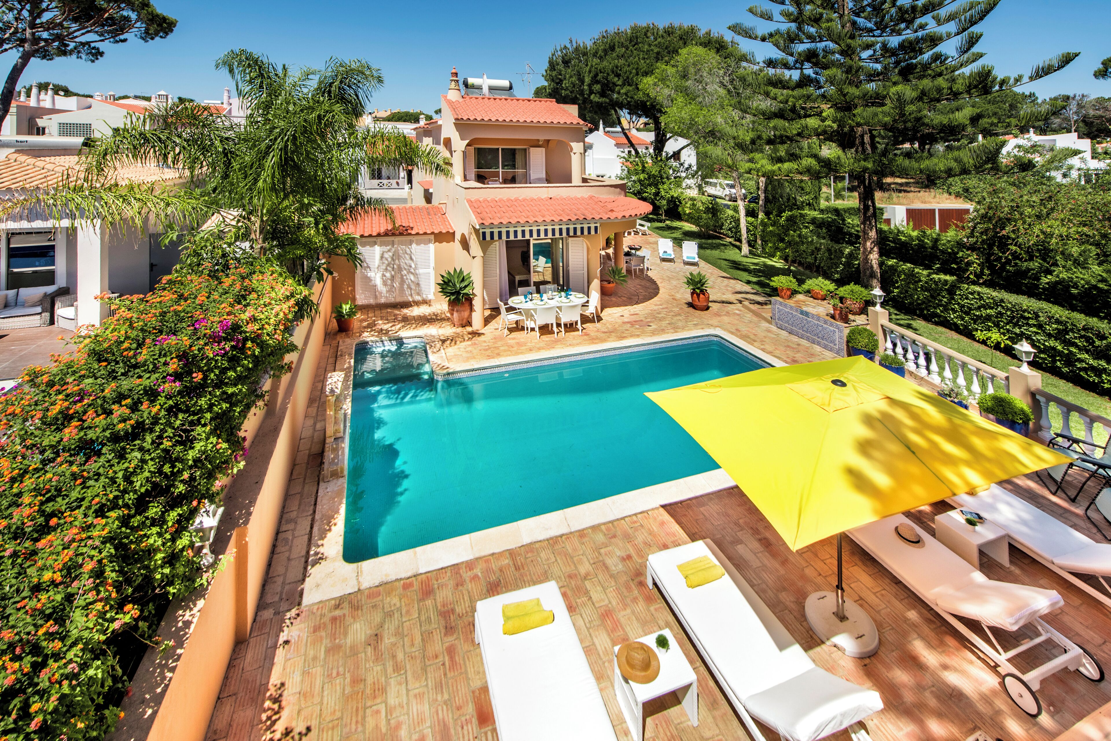 Area piscina con lettini, un ombrellone giallo e vista su una casa con tetto in tegole rosse.