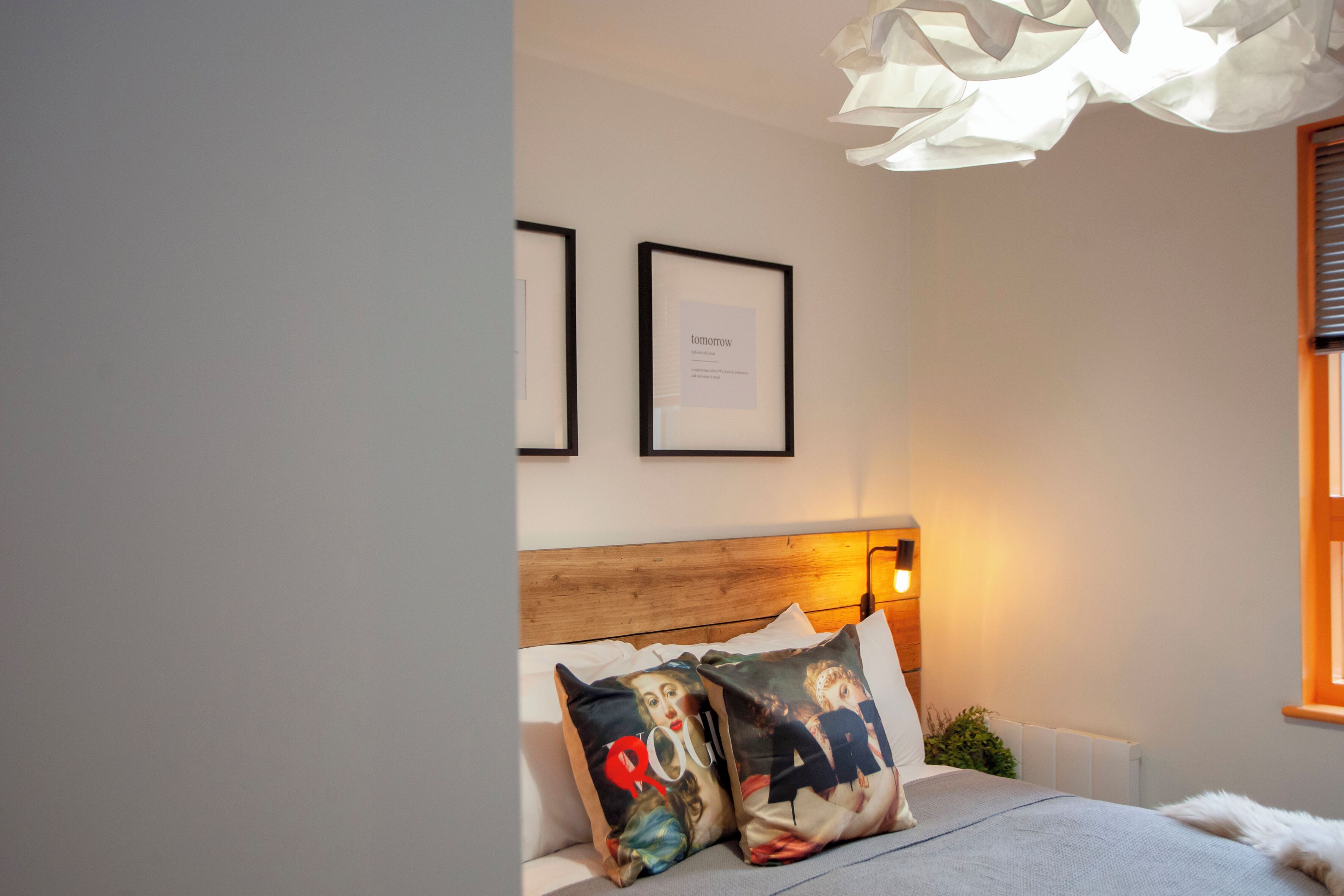 Una camera da letto con una testiera in legno, un letto con cuscini fantasia, quadri appesi alle pareti e una lampada a sospensione.