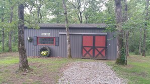 Un cobertizo rústico con puerta roja y un adorno de neumático, rodeado de árboles.