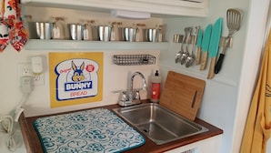 Una cocina compacta con un lavamanos, una tabla de cortar y diferentes utensilios.