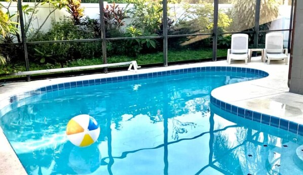 Une piscine avec un bord carrelé, un fauteuil de relaxation et un ballon de plage.