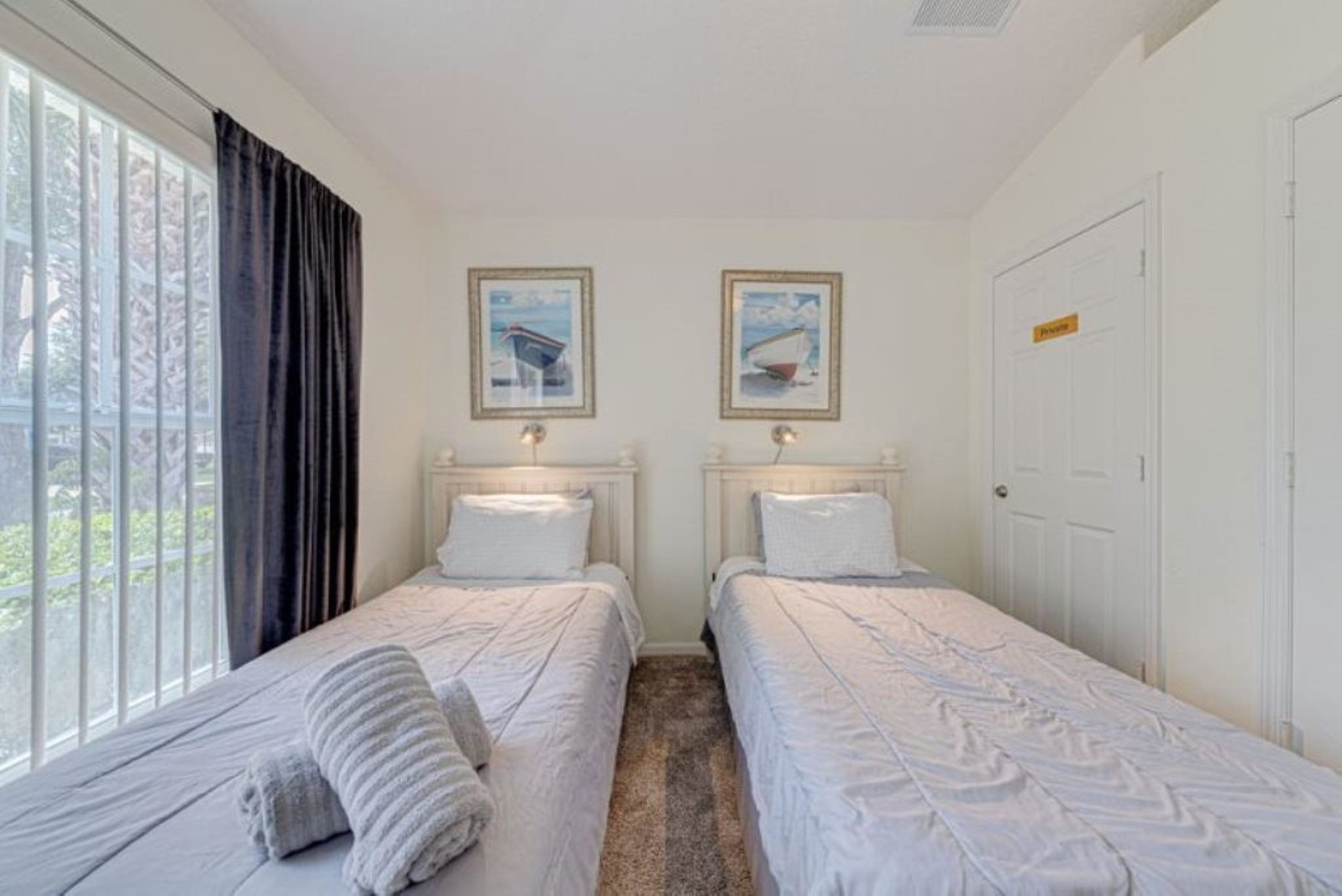 A room with two single beds, a window with curtains, and two framed pictures on the wall.