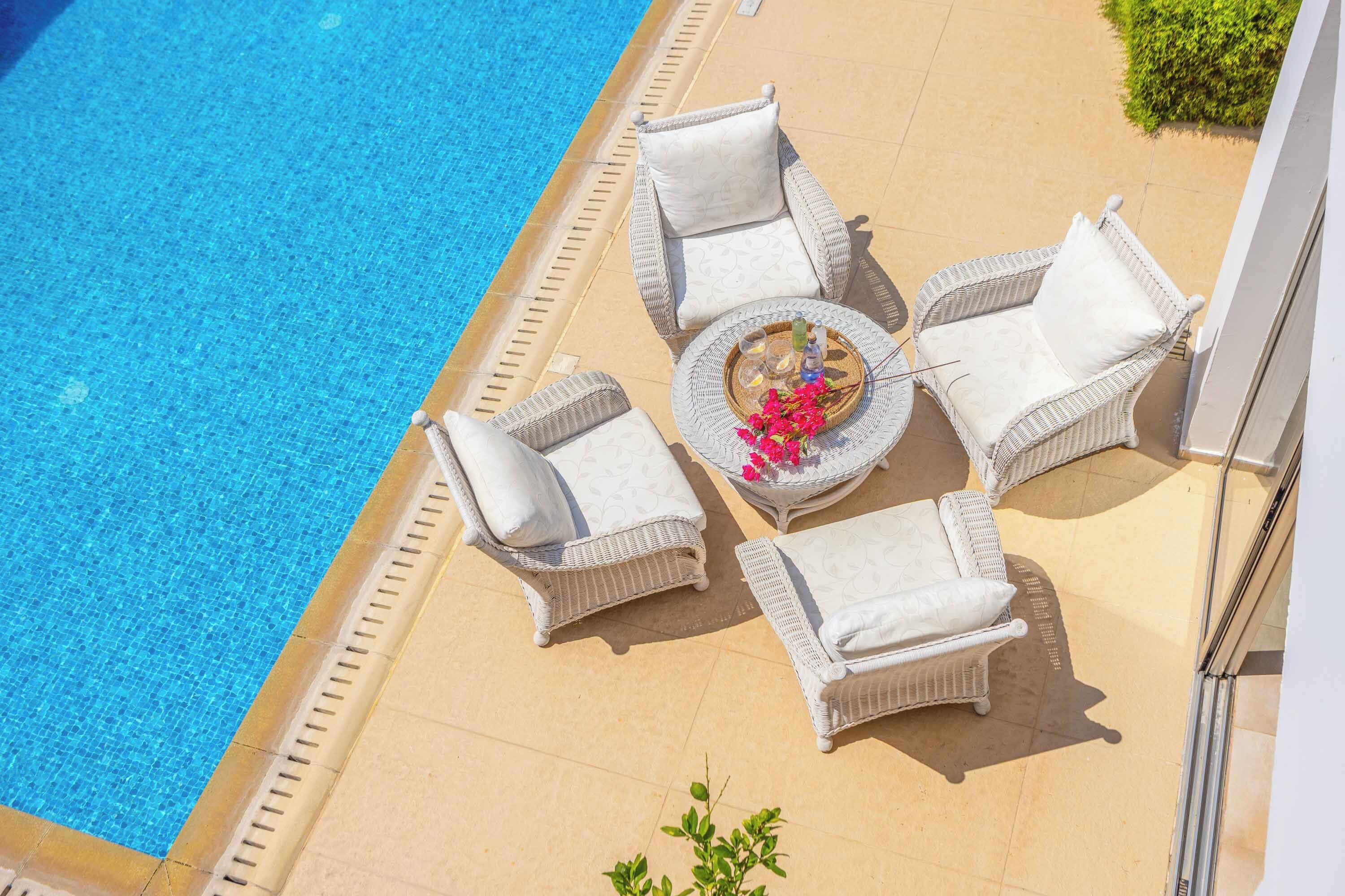 A poolside area with white wicker furniture and a round table with flowers and drinks.