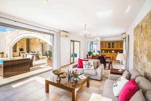 Amplia sala de estar con sofá, mesa de centro y mesa de comedor. Se observa una cocina al fondo con gabinetes de madera y mesa de comedor.