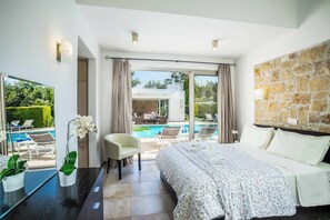 Una habitación de hotel moderna con una cama grande, vistas a una piscina y una pared de piedra.