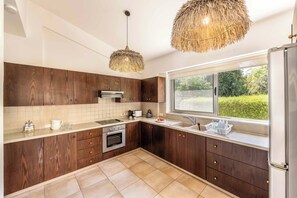 A modern kitchen with wooden cabinets, a built-in oven, a large window, and a hanging light fixture.