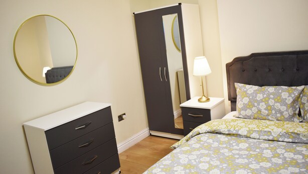 A bedroom with a bed, a dresser, a nightstand, a lamp, and a wardrobe. - Room 2 (Birmingham)
