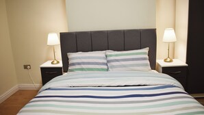 A neatly made bed with a striped bedspread, two bedside tables with lamps, and a dark headboard. - Room 2 (Birmingham)