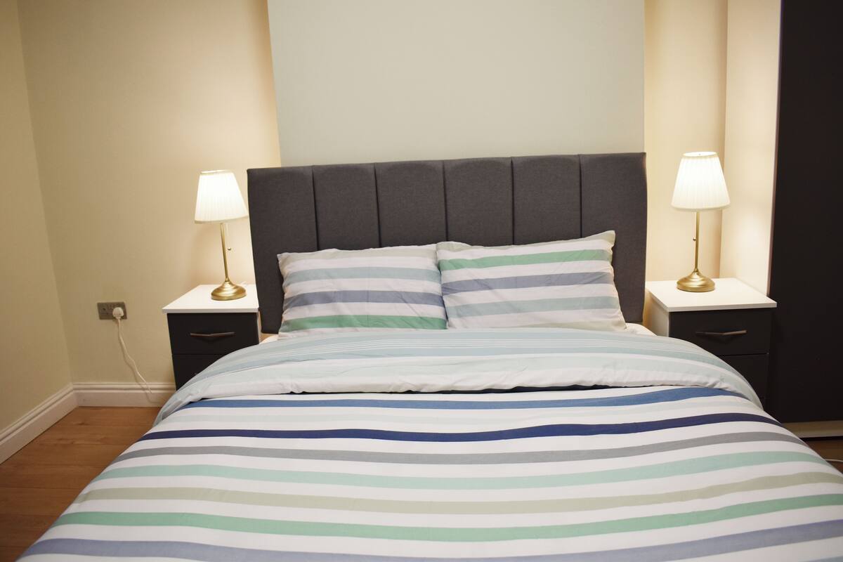 A neatly made bed with a striped bedspread, two bedside tables with lamps, and a dark headboard.