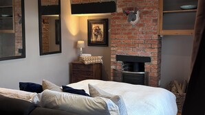 Un dormitorio con chimenea de ladrillo, una cama con ropa de cama blanca, un aparador y un espejo.