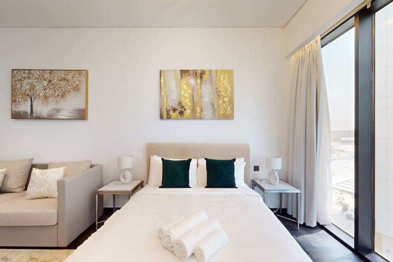 Una habitación de hotel moderna con una cama grande, un sofá, dos mesitas de noche y obras de arte en las paredes.