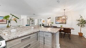 A modern kitchen with granite countertops, wooden cabinets, and a dining area with a table and chairs.