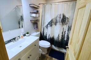 A bathroom with a white sink, a toilet, and a shower curtain with a mountain design. - 3 BDR /1 BA Cabin, Fishing nearby (Soldotna)