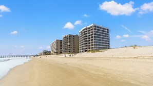 Een strand met een pier die het water in reikt, en meerdere hoge gebouwen op de achtergrond.