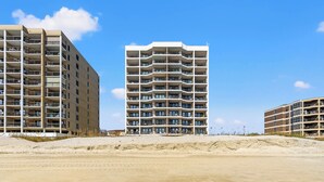 Een hotel aan het strand met meerdere balkons, een zandstrand ervoor en een helderblauwe lucht.