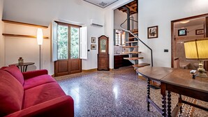 Un amplio espacio habitable con un sofá rojo, una mesa de comedor de madera y una escalera que sube a un piso superior.