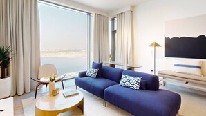 A modern hotel room with a large window, a sofa, a coffee table, and a lamp.