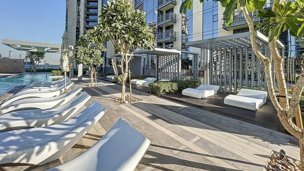 A rooftop pool area with lounge chairs, a small tree, and a building in the background.