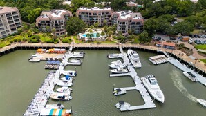 A marina with various boats docked, surrounded by a residential area with multi-story buildings. - Sunset Rentals | Yacht Club 7548 | Shelter Cove (Hilton Head Island)