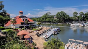 A marina with boats docked, a building with a red roof, and a river. - Sunset Rentals | Yacht Club 7548 | Shelter Cove (Hilton Head Island)