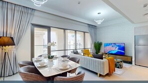 A modern living room with a dining area, large windows, a flat-screen TV, and a sofa.