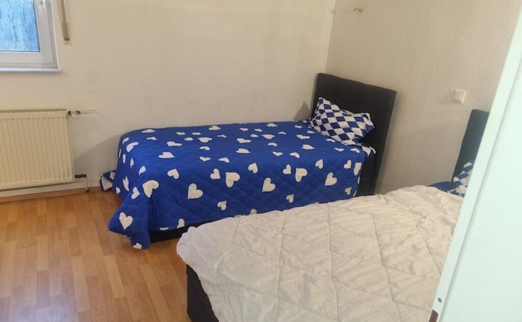 Quarto com cama coberta por um cobertor azul com padrões de corações brancos, um edredom acolchado branco e uma almofada xadrez.
