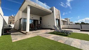 A modern house with a patio area, a barbecue grill, and a swimming pool.
