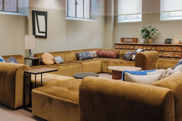 A modern living room with a sectional sofa, a small table, and a potted plant. - De Plesman Hotel The Hague (The Hague)