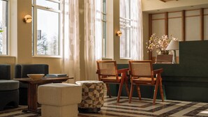 A cozy room with a sofa, two wooden chairs, a small table, and a patterned ottoman. - De Plesman Hotel The Hague (The Hague)
