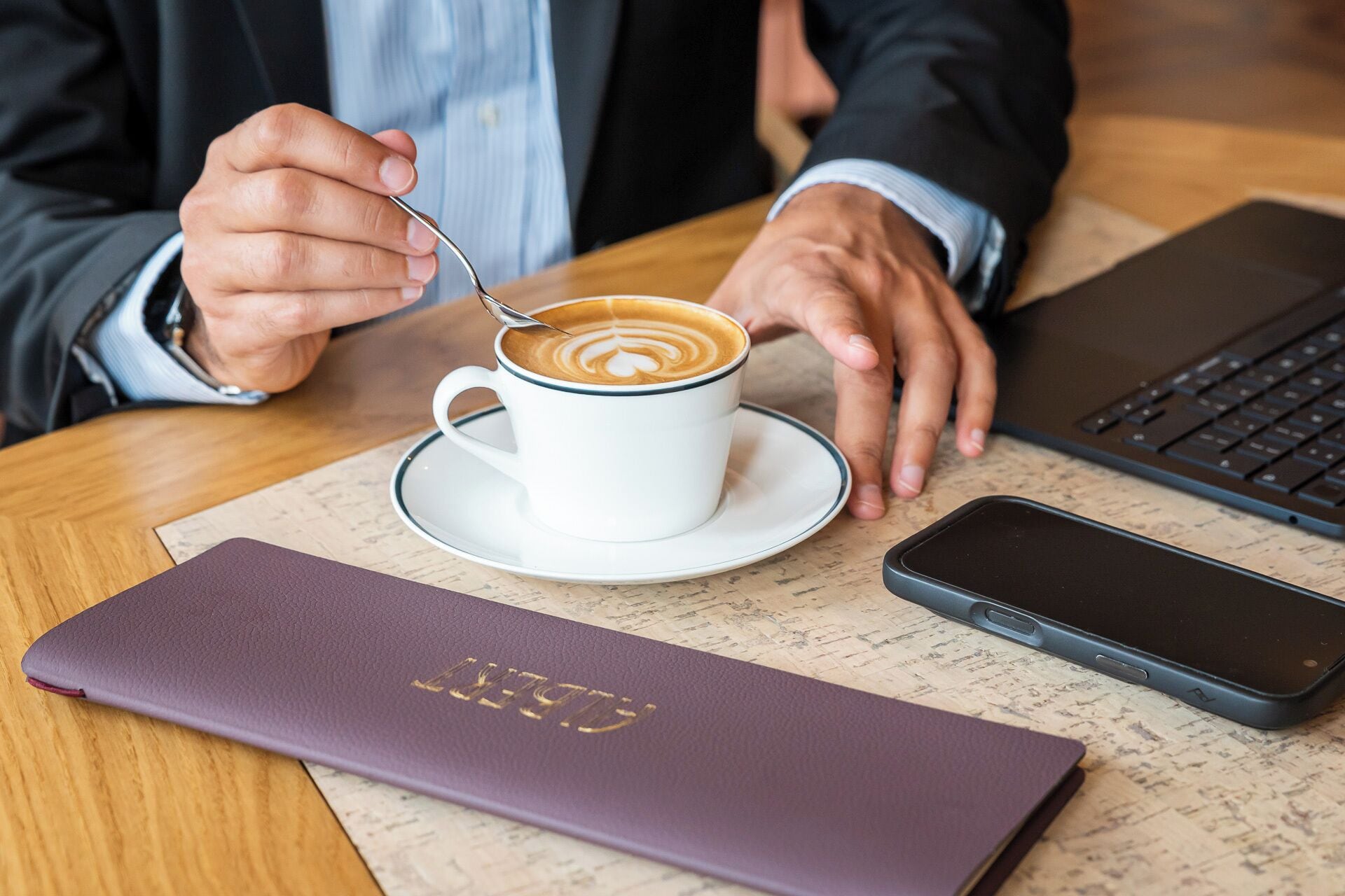 Una persona sentada a una mesa con una taza de café, una computadora portátil y un teléfono inteligente.