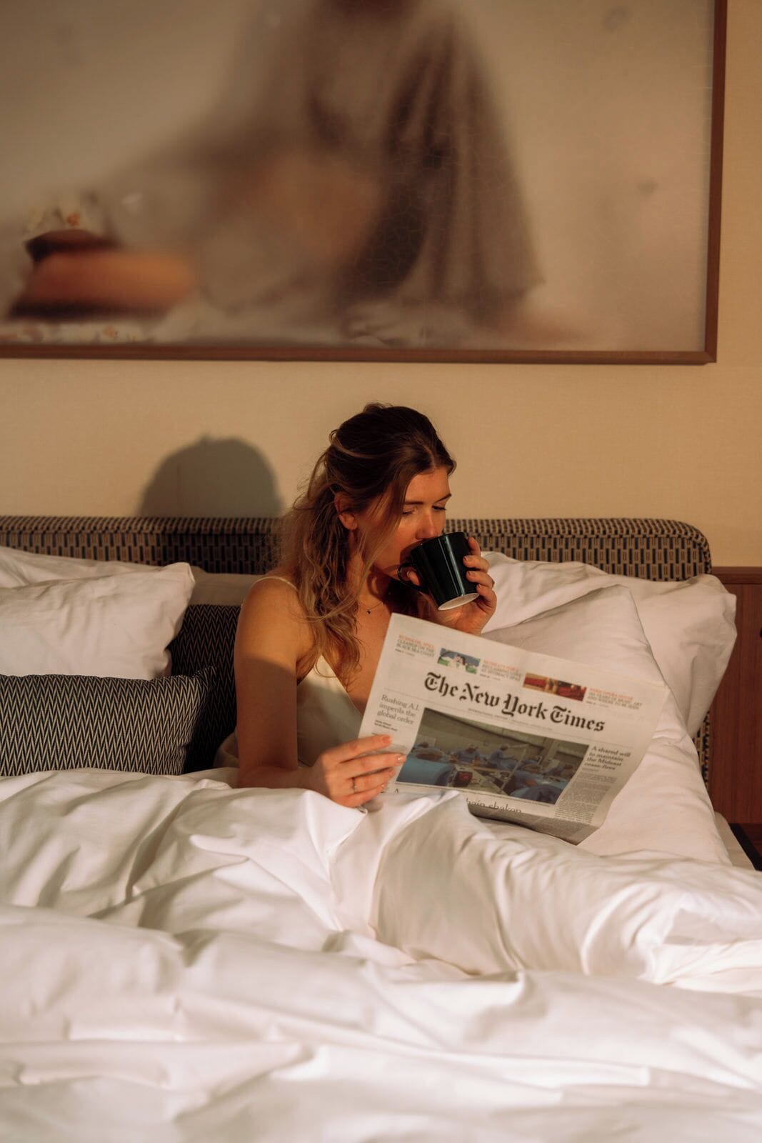 A person lying on a bed with a newspaper, reading.