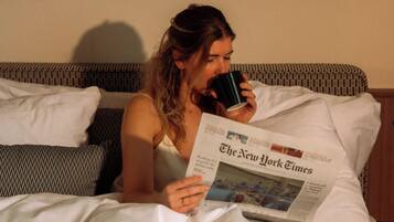 A person lying on a bed with a newspaper, reading.