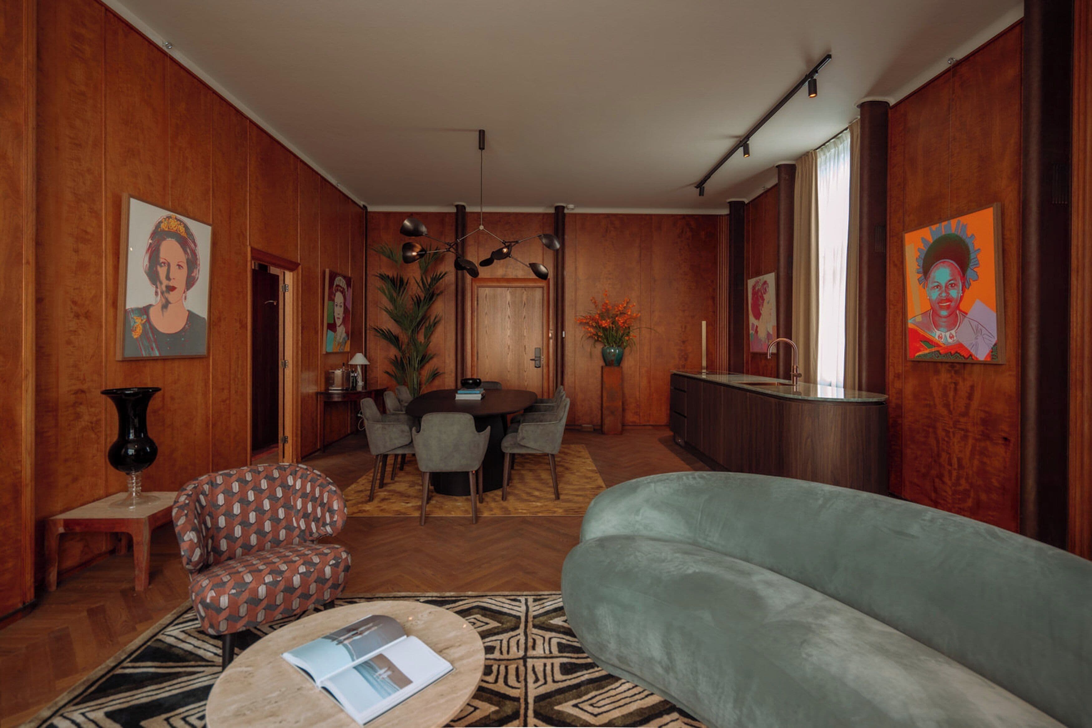 A modern living room with a sofa, a coffee table, a dining table with chairs, and a kitchen area with a sink and cabinets.