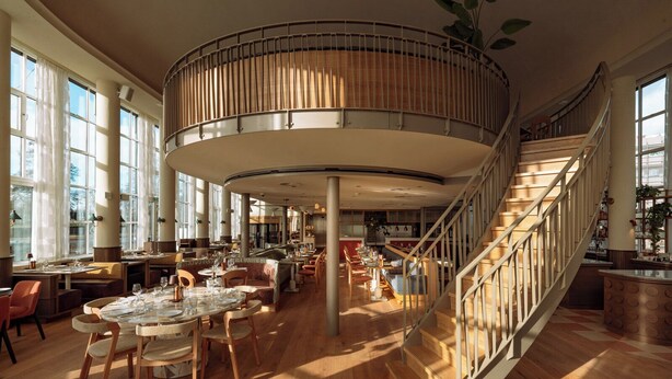 A spacious restaurant with a central circular seating area, wooden flooring, and a staircase with a railing. - De Plesman Hotel The Hague (The Hague)