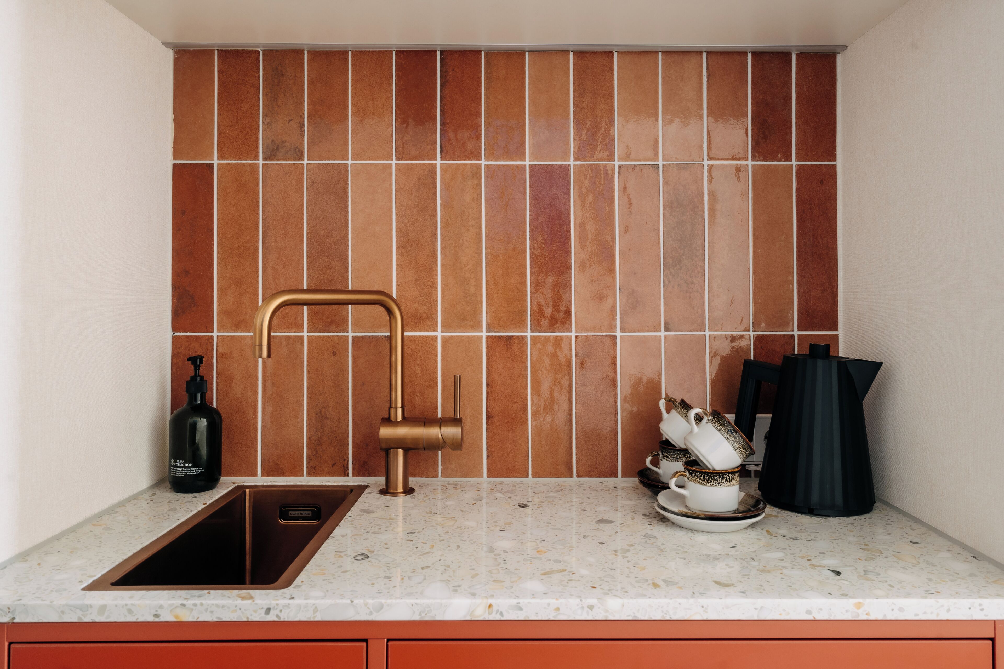Una cocina con un lavamanos, un grifo, una cafetera y una botella de jabón para manos.