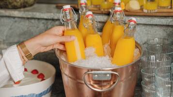 Een hand houdt een fles sinaasappelsap vast, met meerdere flessen in een koperen emmer vol ijs.