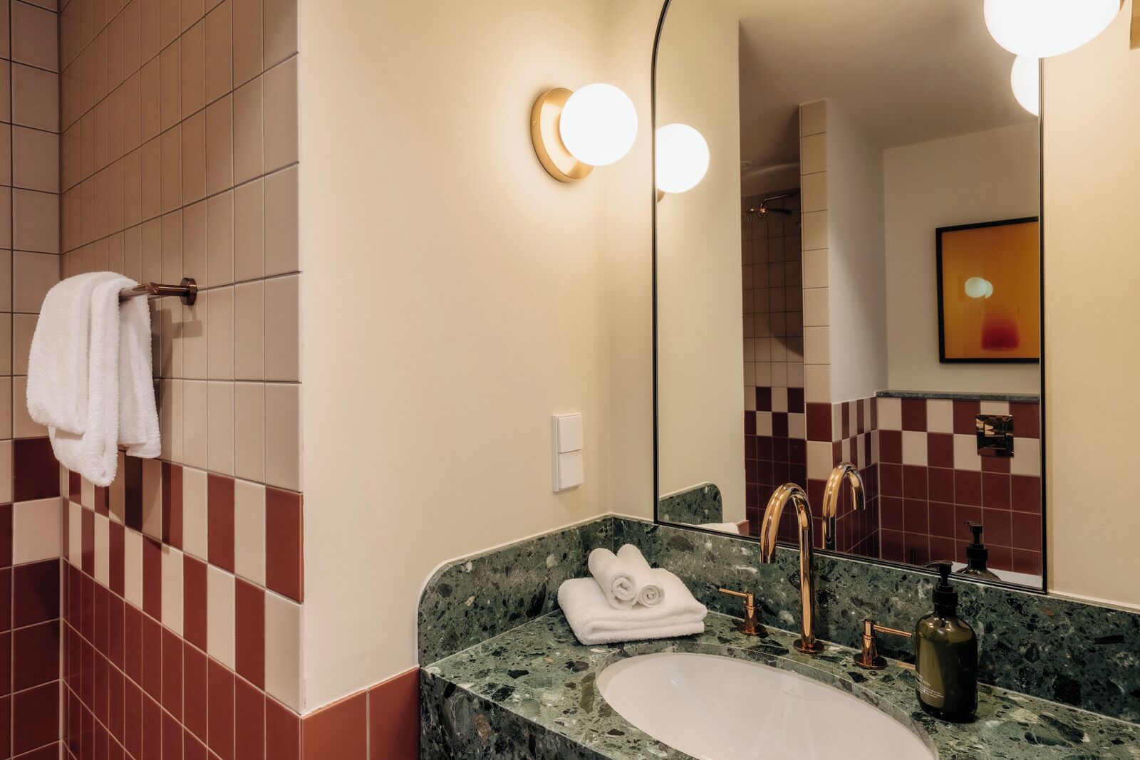 Un baño moderno con lavamanos de mármol, grifos dorados y un espejo grande.
