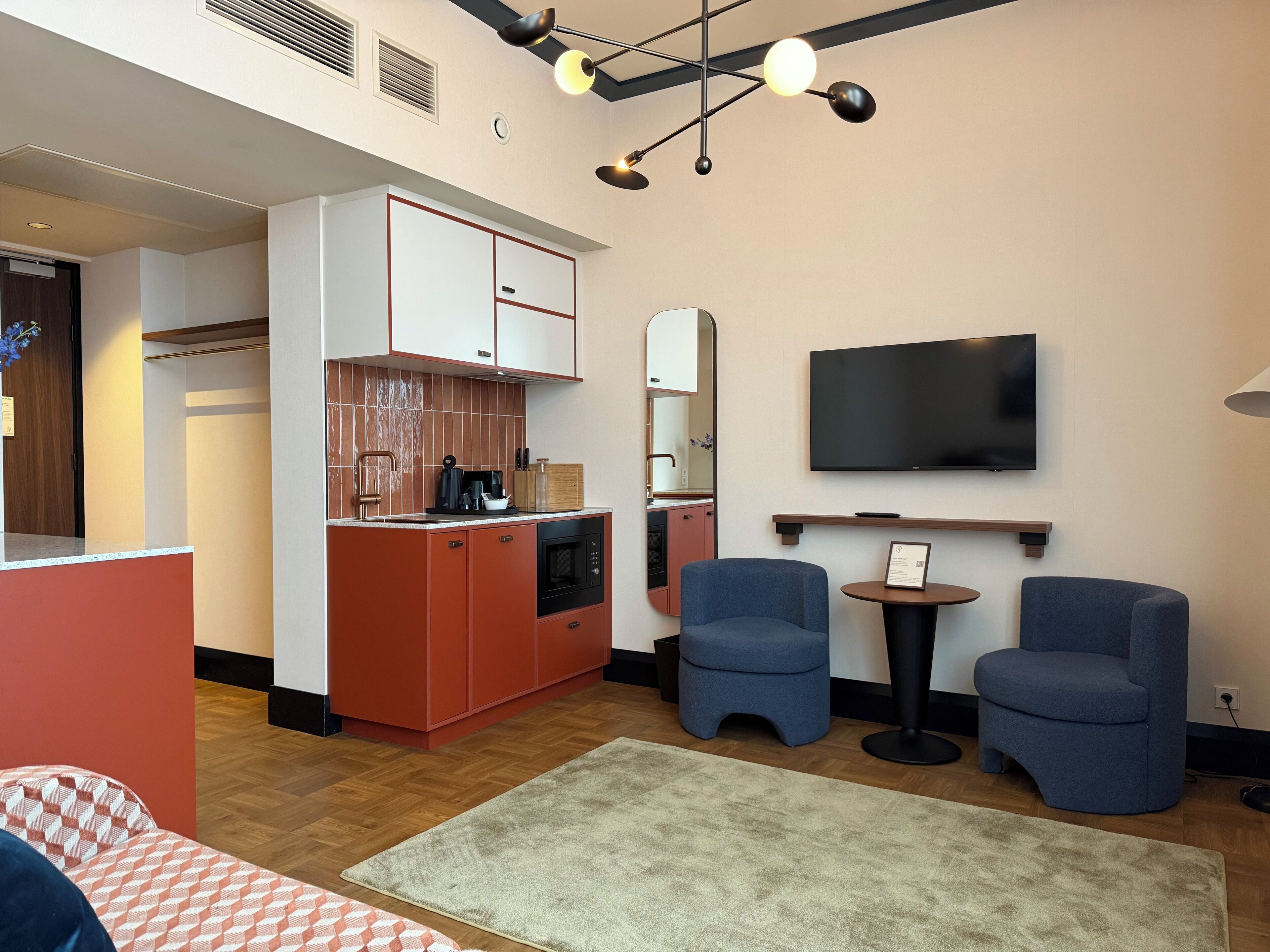 A compact living space with a kitchenette, a flat-screen TV, and two seating areas.