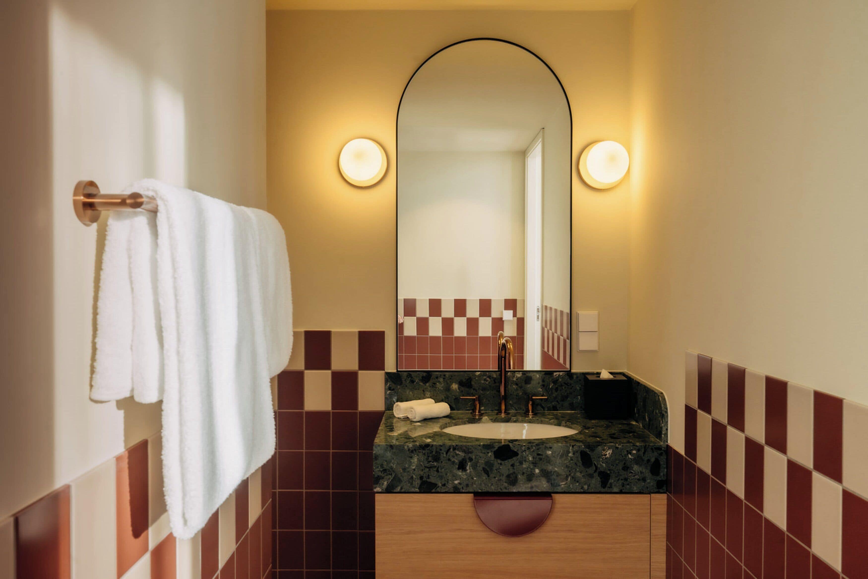 Un baño con lavamanos, espejo y toallero.