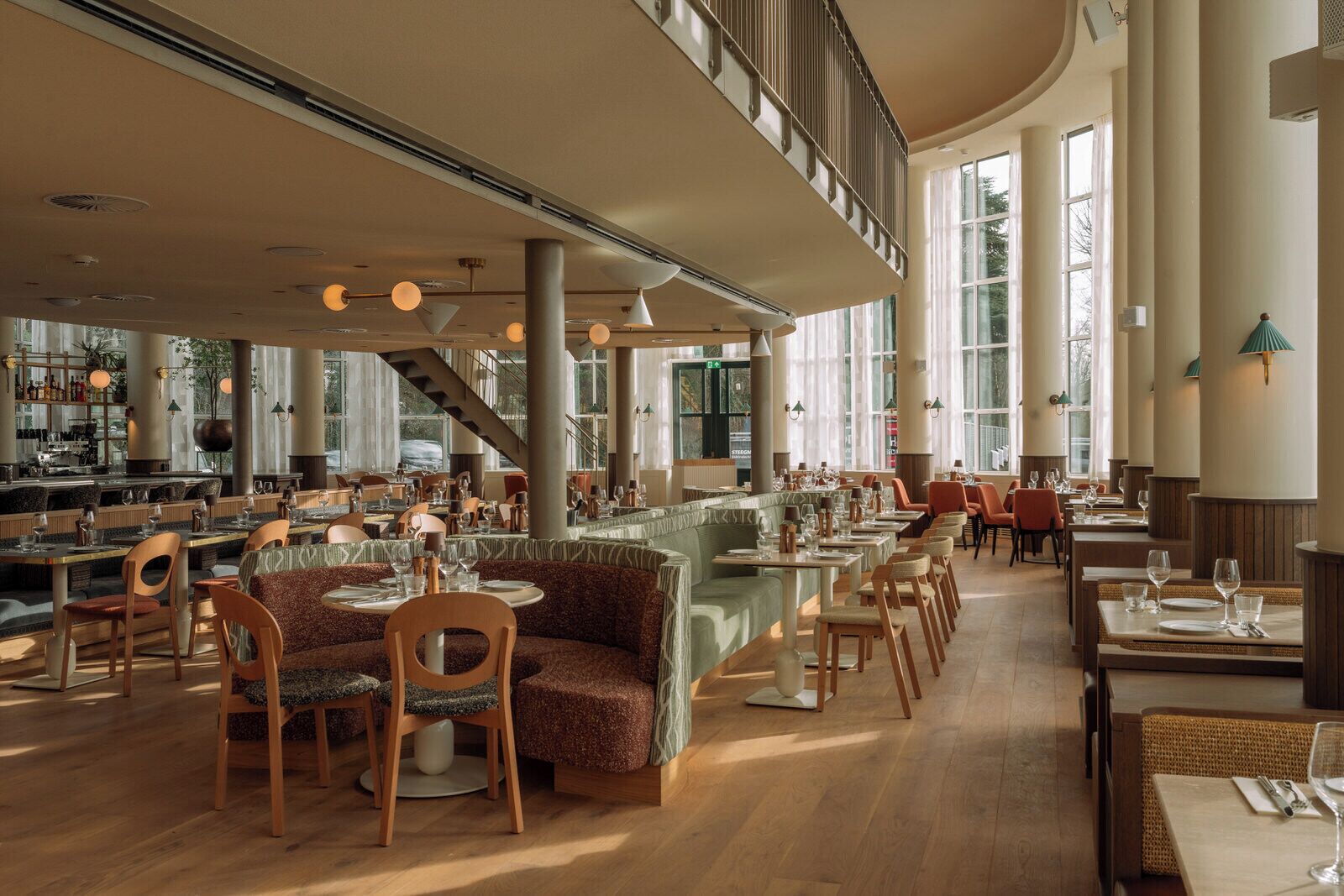 Ein geräumiges Restaurant mit hohen Decken, großen Fenstern und verschiedenen Sitzmöglichkeiten, darunter Sitzecken und Tische.