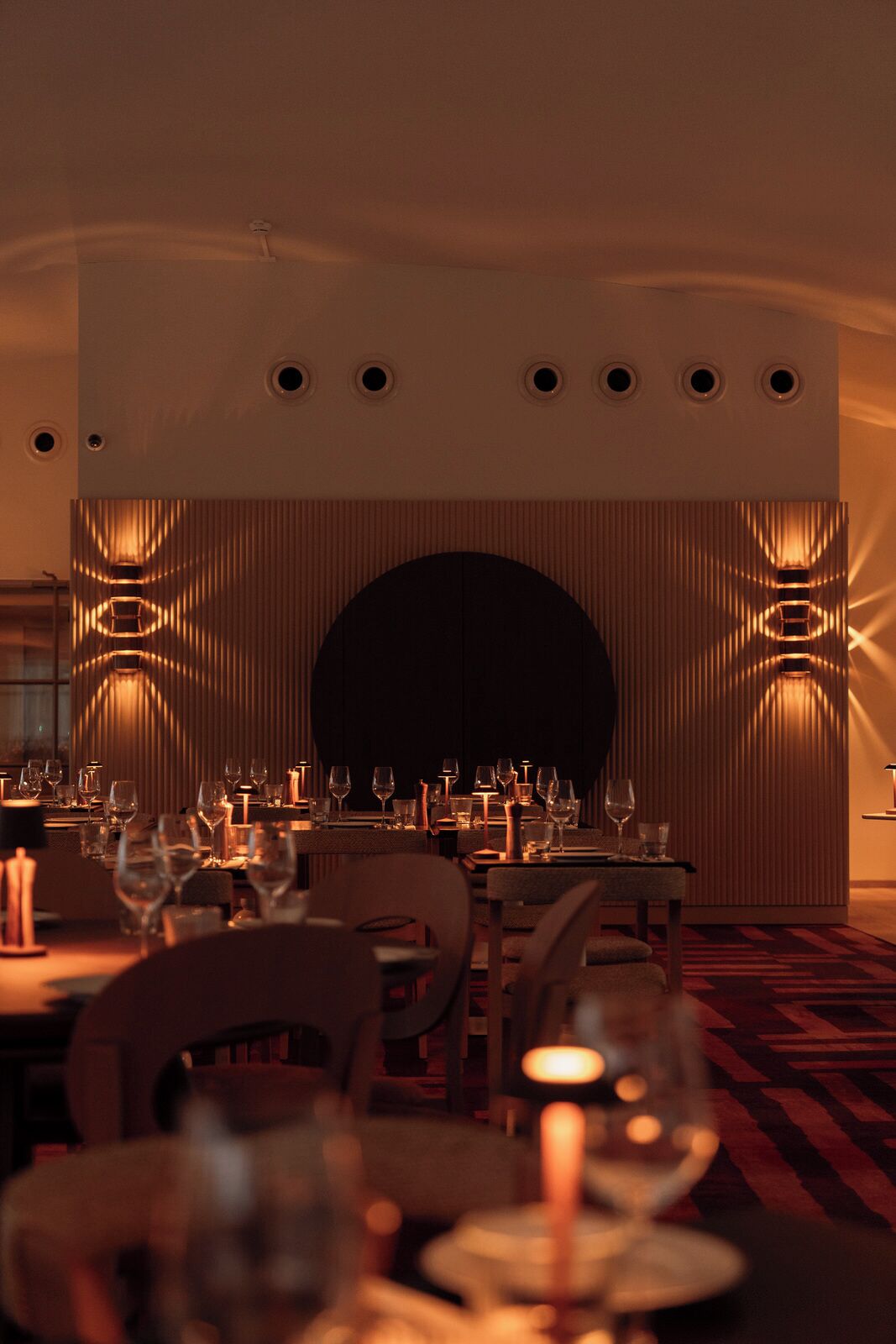 A dimly lit restaurant with tables set for dining, featuring a central dark arch and warm lighting.