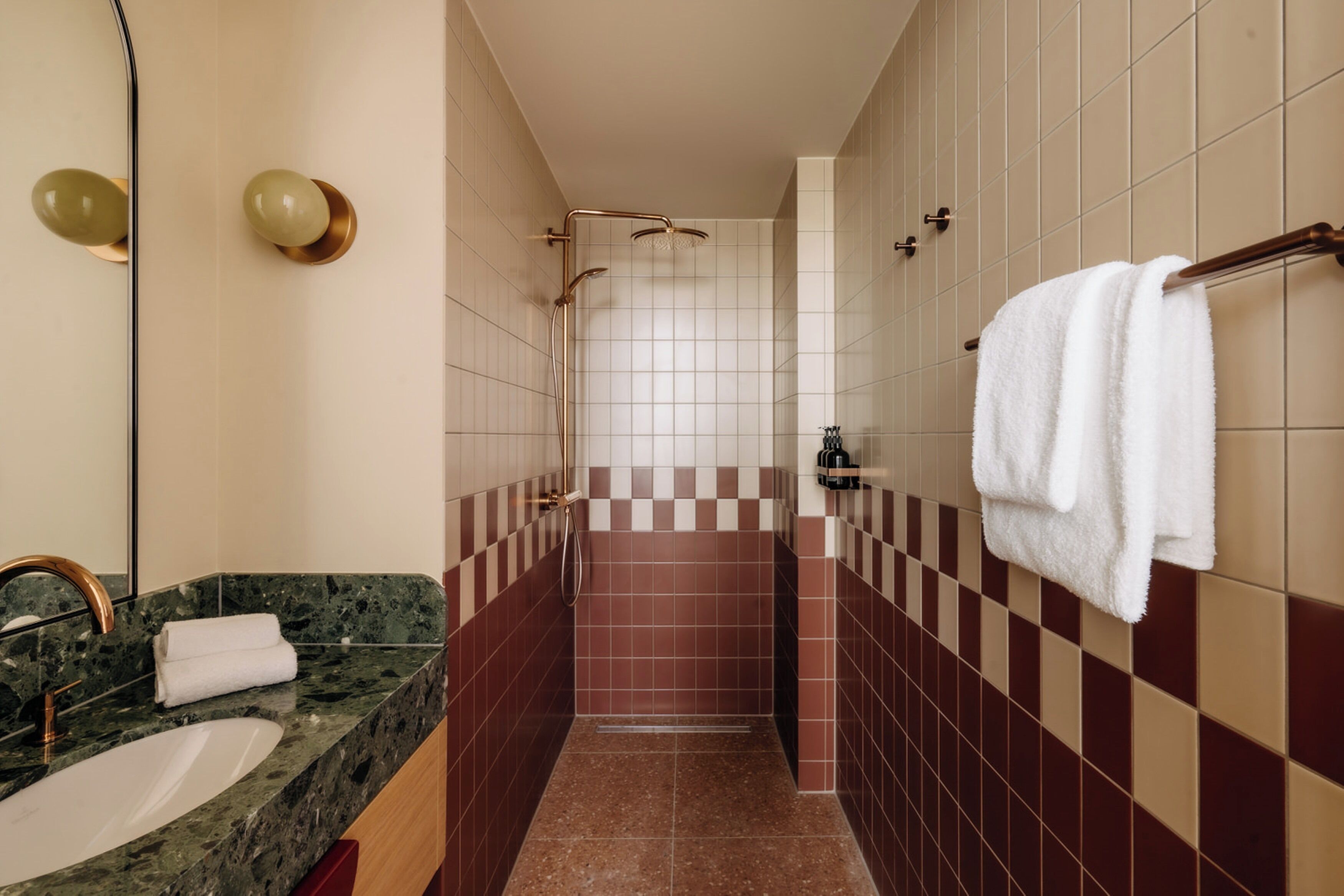 Un baño con lavamanos de mármol, un perchero con una toalla blanca y una zona de ducha con un diseño de baldosas a cuadros.