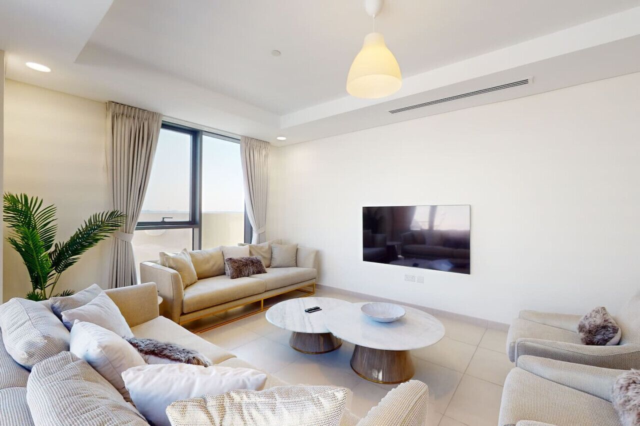 A modern living room with a sofa set, a round coffee table, and a flat-screen TV mounted on the wall.
