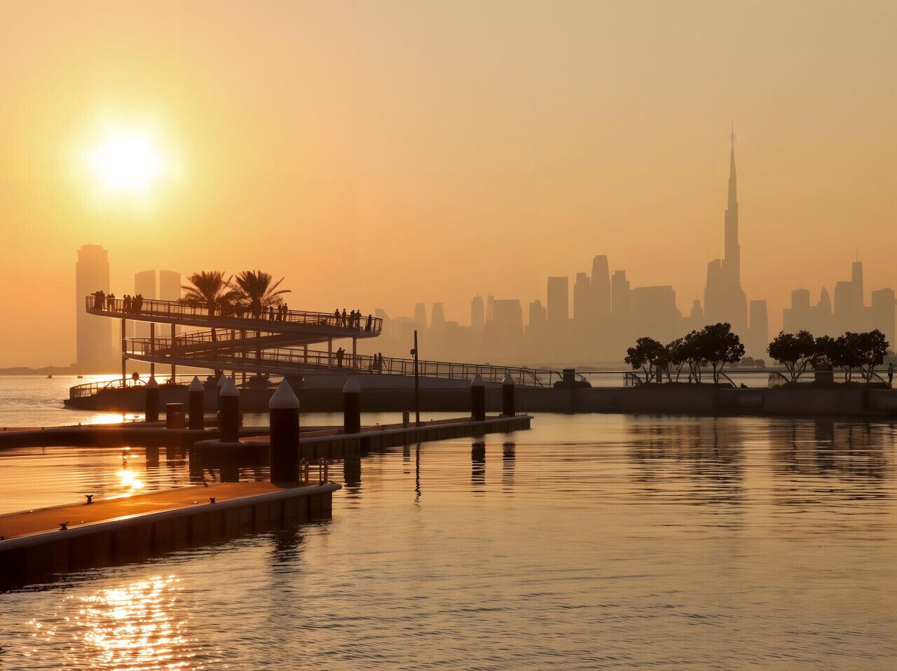A waterfront promenade with a viewing platform, calm water, and a city skyline in the background.