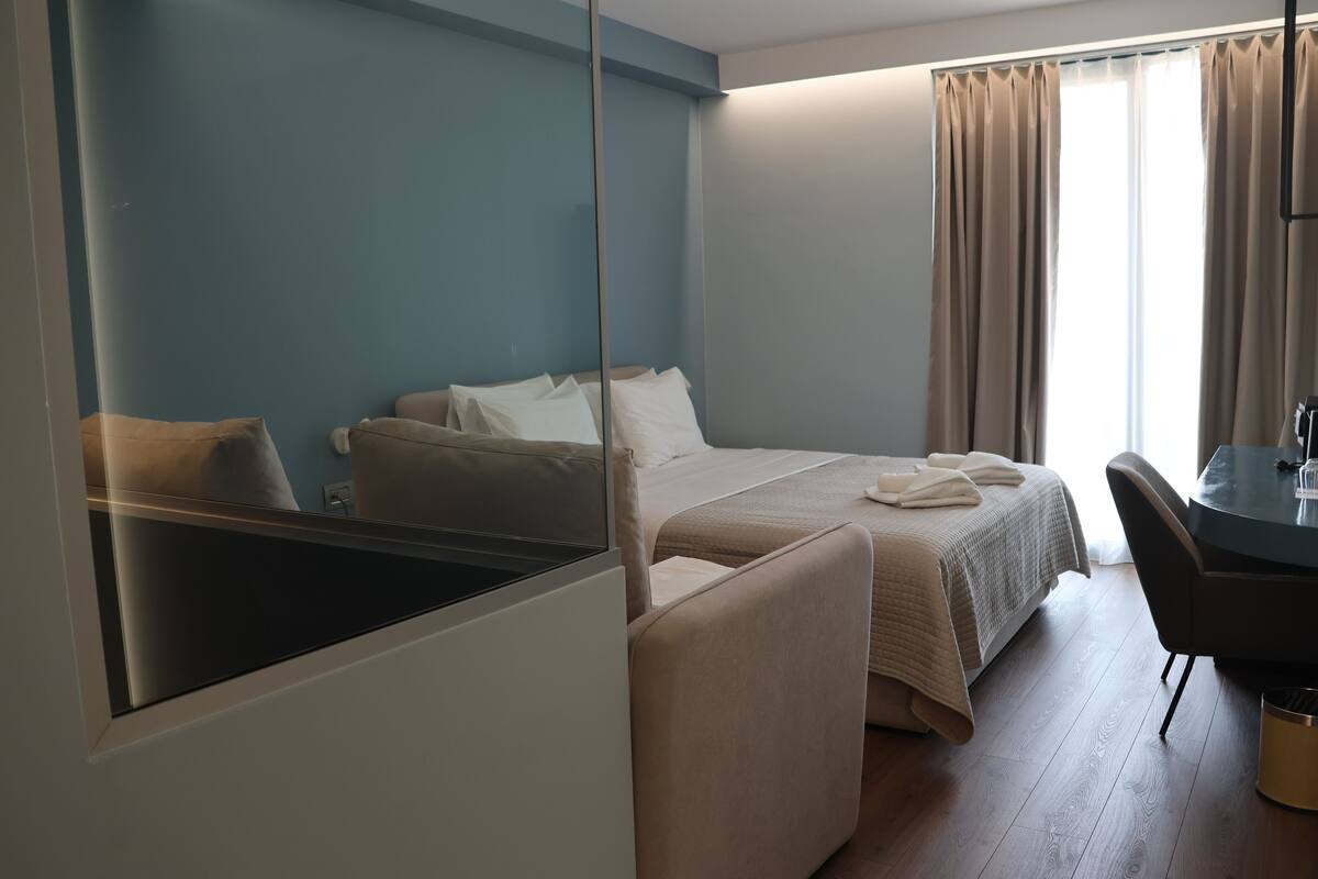 Habitación de hotel con cama, una silla, una mesa y una ventana con cortinas.