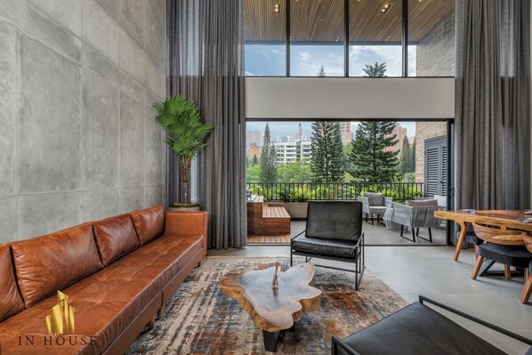 A modern living room with a leather sofa, a wooden coffee table, and a view of the city through large windows. - Elevated Living: Balcony, AC - Morph 702 (Medellín)